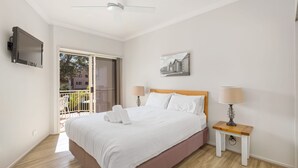 Ein Hotelzimmer mit Bett, Wandfernseher, einem Gemälde und einem Balkon mit Stuhl.