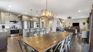 A spacious kitchen with modern appliances, a wooden dining table, and a chandelier. - Stillwater - Indoor pool & lake views (Branson)