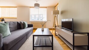 A modern living room with a sofa, coffee table, TV, and a lamp. - The Clerkenwell Apartments. (London)