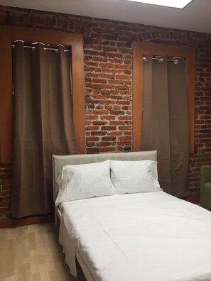 A room with a brick wall, a bed with white bedding, and curtains.
