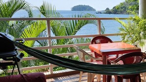 A balcony with a hammock, a table, and chairs overlooking a body of water and a distant island. - BEAUTIFUL APARTMENT IN FRONT OF THE SEA (Portobelo)