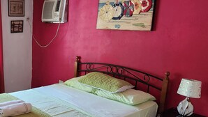 A room with a bed, a nightstand with a lamp, a painting on the wall, and an air conditioner. - BEAUTIFUL APARTMENT IN FRONT OF THE SEA (Portobelo)