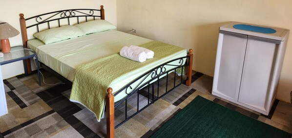 A single bed with a green bedspread, a white towel on the bed, a bedside table with a lamp, and a cabinet with a blue mat on top. - BEAUTIFUL APARTMENT RIGHT BY THE OCEAN (Portobelo)