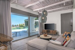 A modern living room with a large TV, comfortable seating, and a view of a swimming pool. - Villa Krini Myth - Three Bedroom Villa, Sleeps 6 (Rhodes)