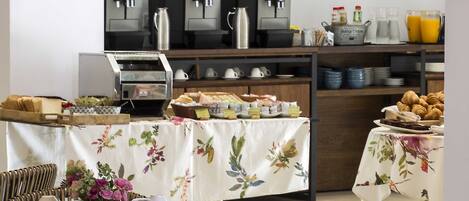 Un área de panadería con máquinas de café, una mesa de buffet y sillas de mimbre.