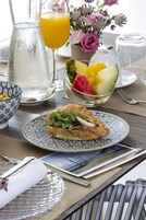 Una mesa de desayuno con un croissant, un bol de fruta, una jarra y un vaso de zumo de naranja.