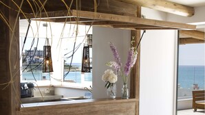 A wooden bar area with stools, a wicker basket, and a view of the sea.