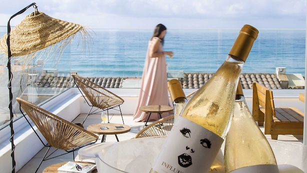 A balcony with wicker chairs, a table with a bottle of champagne, and a view of the sea.