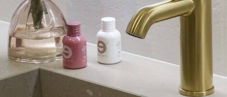 Un lavamanos con grifo dorado, un florero con flores blancas y dos botellas pequeñas sobre la encimera.
