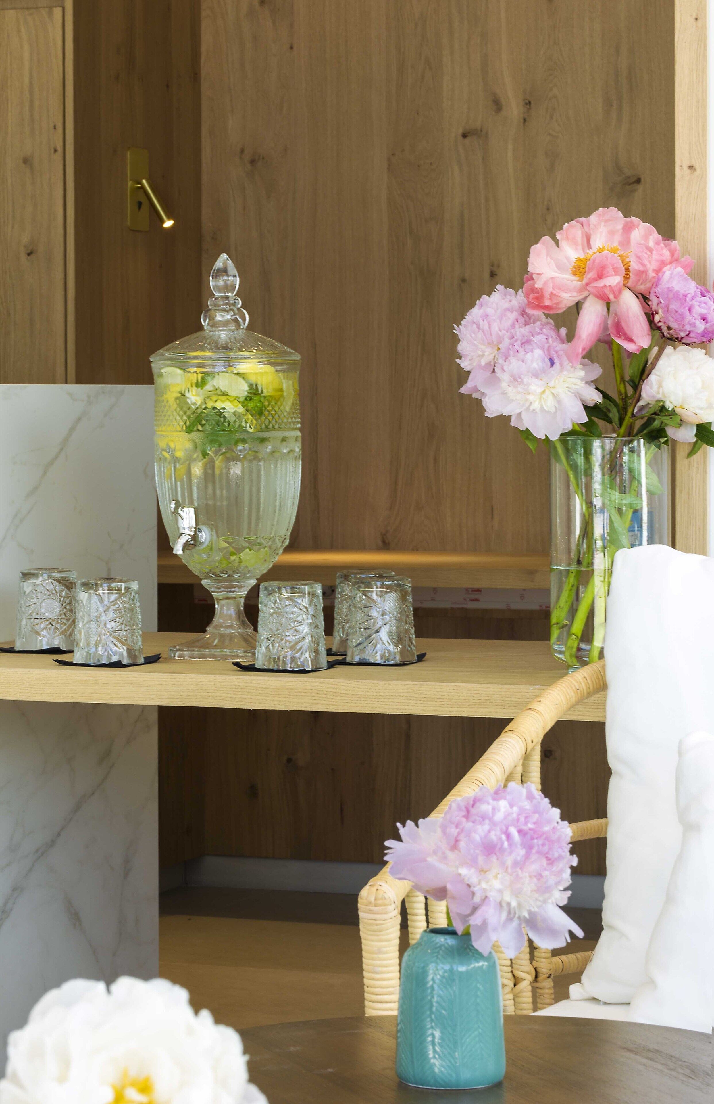 Ein Holzeinrichtung mit einer Marmorsäule, einer großen Glas-Punschschale mit Blumen und einem Korbstuhl.