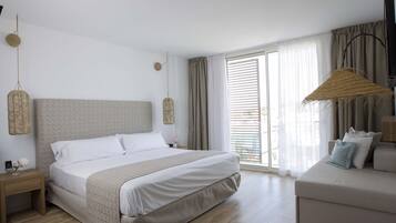 Une chambre moderne avec un grand lit, une table de chevet, une petite table ornée d’un vase, un canapé et une grande fenêtre avec des rideaux.