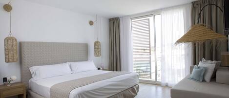 A modern bedroom with a large bed, a bedside table, a small table with a vase, a sofa, and a large window with curtains.