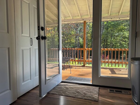 An open sliding glass door leading to an outdoor deck with a wooden railing and a chair.