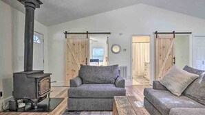 A living room with a wood-burning stove, two sofas, a coffee table, and a view of a barn through a sliding door.