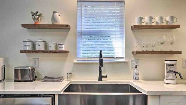 A modern kitchen with a stainless steel sink, a toaster, a coffee maker, and shelves with kitchenware.