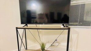 A flat-screen TV on a black metal TV stand with a small potted plant on the shelf.