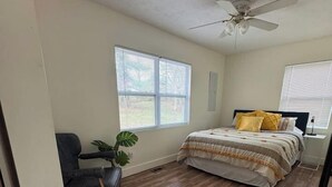 A bedroom with a bed, a ceiling fan, a window, and a chair.