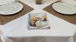 Ein Esstisch, gedeckt mit zwei Tellern, einer Vase mit getrockneten Blumen und einem Notizbuch.