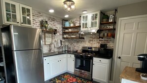 Una cocina con armarios blancos, un refrigerador de acero inoxidable, una estufa y un microondas. Hay una alfombra decorativa en el suelo.