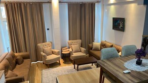 A modern living room with a sofa set, two armchairs, a coffee table, and a dining table with a placemat. - Beautiful 3-bedroom House With Sea View and Garden (Kusadasi)