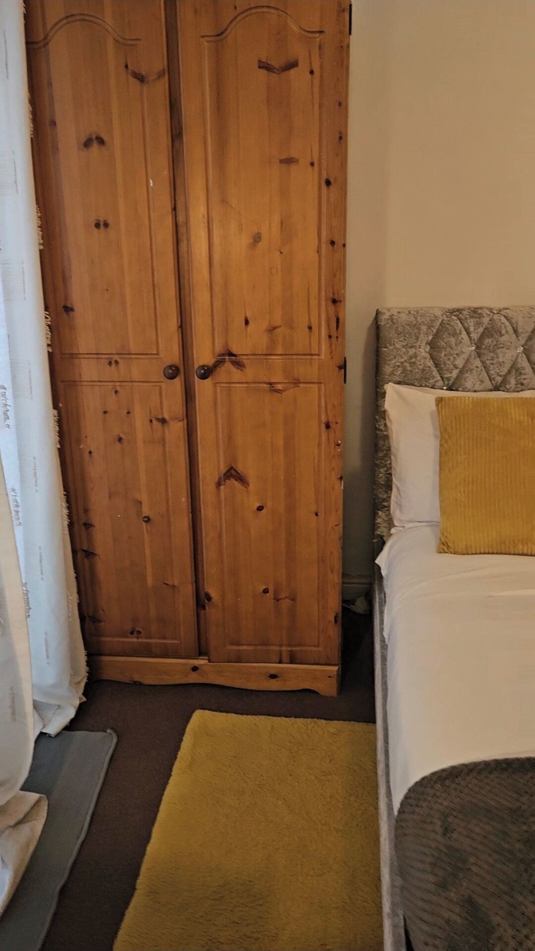 Ein Schlafzimmer mit einem Holzschrank, einem Bett mit Kopfteil und einem gelben Teppich.