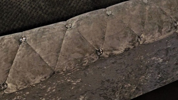 Una cama bien hecha con cabecera gris, una lámpara de noche y una mesita con lámpara.