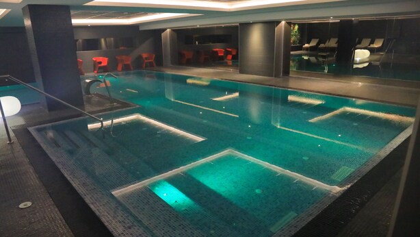 A large indoor swimming pool with clear water, surrounded by dark walls and red chairs. - Az Hotels Grand Oran (Es Senia)