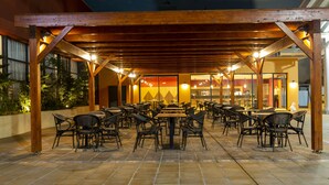 An outdoor dining area with wooden pergola, tiled flooring, and multiple tables and chairs. - Az Hotels Grand Oran (Es Senia)