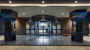 A modern hotel entrance with a revolving door, a glass elevator, and a reception desk. - Az Hotels Grand Oran (Es Senia)
