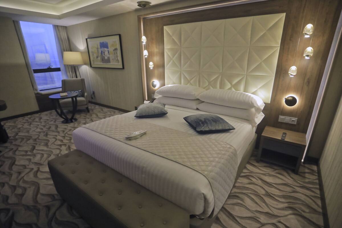 A hotel room with a large bed, a bedside table, a chair, a desk, and a window with curtains.