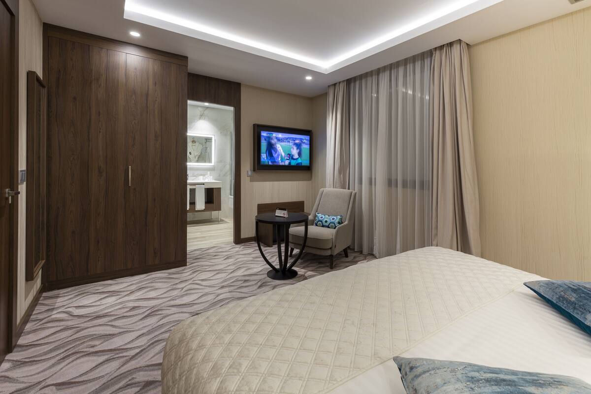 A hotel room with a large bed, a television mounted on the wall, a chair, and a small table.