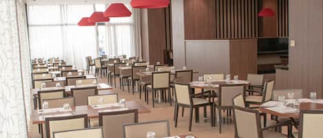 A spacious dining area with multiple tables and chairs, red pendant lights, and a modern interior design.