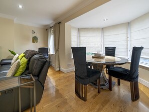 A modern living room with a round dining table, black upholstered chairs, a leather sofa, and a large window with blinds.