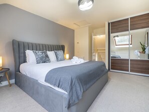 A modern bedroom with a large bed, a bedside table, a mirror, and a sliding door leading to a bathroom.