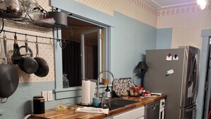 Ett kompakt kök med en bänkskiva i trä, ett kylskåp i rostfritt stål och en hängande hylla för kastruller.