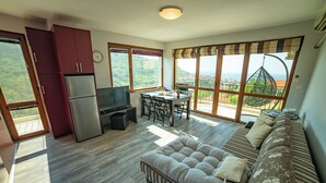 Uma sala ampla com sofá, mesa de jantar e cozinha com geladeira.