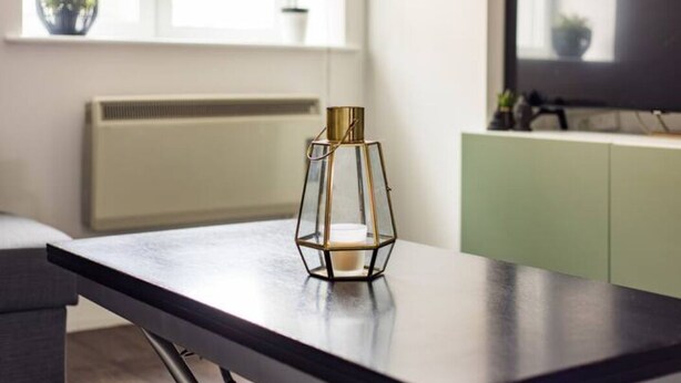 A modern room with a dark wooden table, a geometric glass candle holder, and a view of a window with plants. - The Waterloo Flats (London)