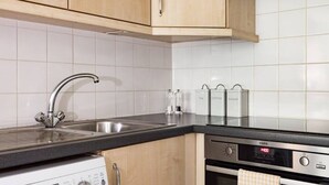 A kitchen with wooden cabinets, a stainless steel sink, a coffee machine, and an oven. - The Waterloo Flats (London)