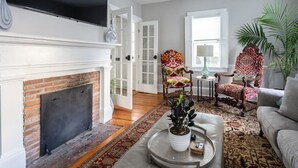 A living room with a fireplace, a television mounted above it, and two patterned armchairs.