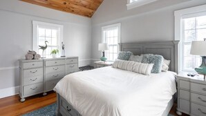 A bedroom with a large bed, two nightstands, a dresser, and a wooden ceiling.
