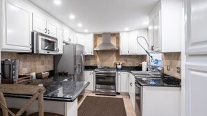 A modern kitchen with white cabinets, stainless steel appliances, a granite countertop, and a wooden chair.