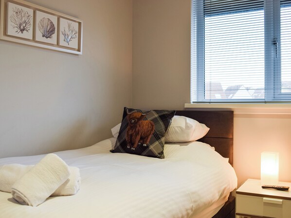 A neatly made bed with white linens, a pillow with an animal print, and a bedside table with a remote control.