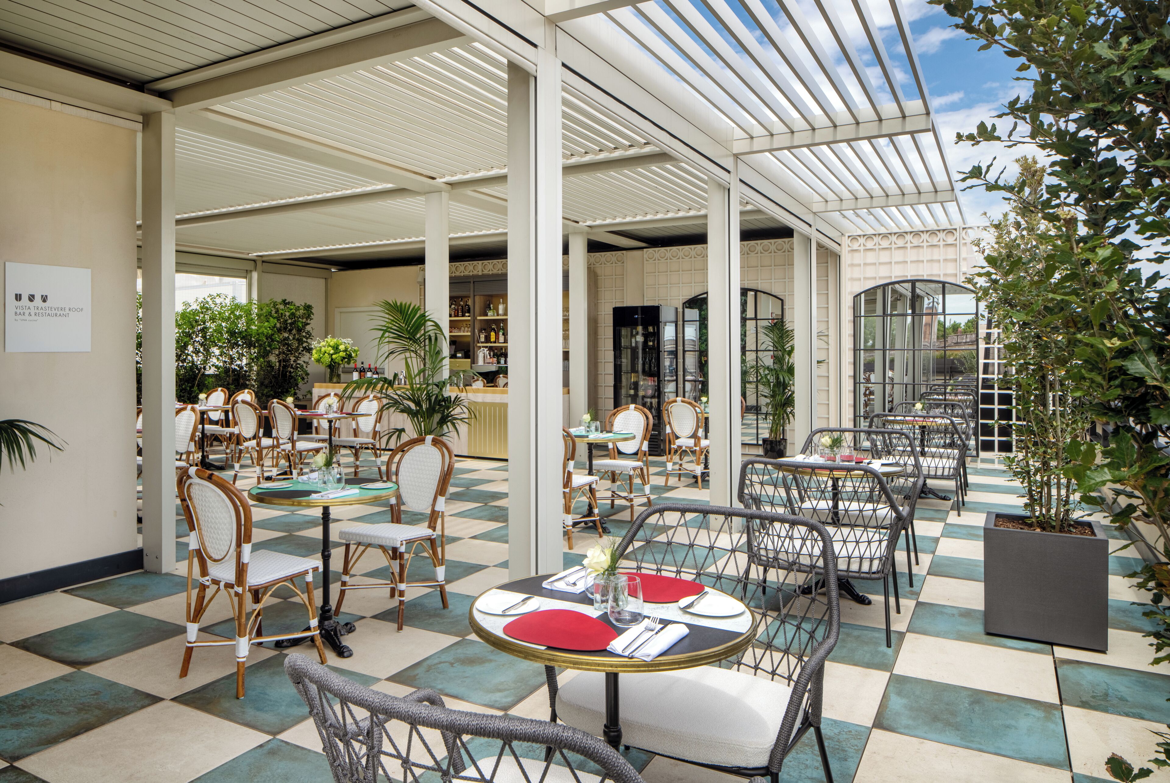 A spacious indoor patio with checkered flooring, wicker chairs, and tables set for dining.