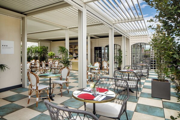 A spacious indoor patio with checkered flooring, wicker chairs, and tables set for dining. - Trastevere Roma | UNA Esperienze | Preferred Hotels and Resorts (Rome)