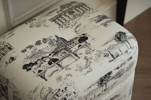 A round ottoman with a black and white print of a cityscape, including buildings and trees.