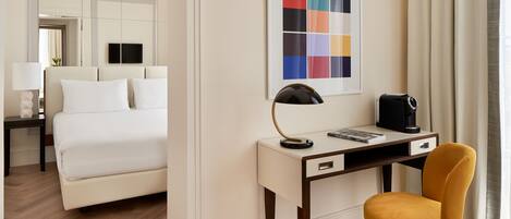 A hotel room with a bed, a desk with a chair, a coffee maker, and a framed color palette on the wall.