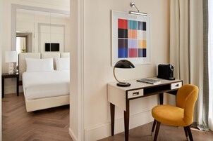 A hotel room with a bed, a desk with a chair, a coffee maker, and a framed color palette on the wall.