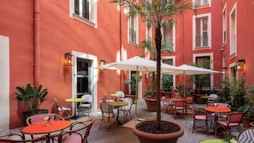 Una terrazza esterna con sedie a scacchi rossi e bianchi, tavoli rotondi e piante in vaso.