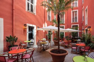Un patio al aire libre con sillas a cuadros rojos y blancos, mesas redondas y plantas en macetas.