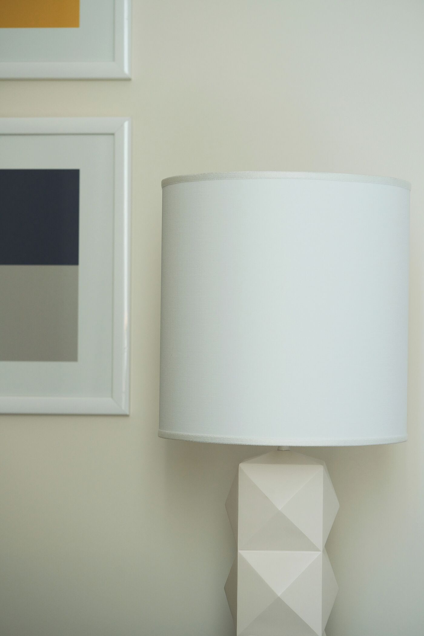 A modern lamp with a geometric base and a white lampshade on a wall.
